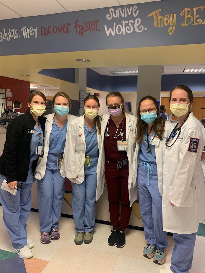 six pediatric residents posing in full uniform in hospital unit